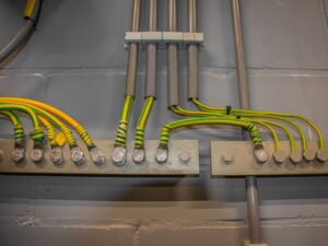Sistema de aterramento em parede com fios amarelos e verdes conectados, demonstrando instalação elétrica segura.