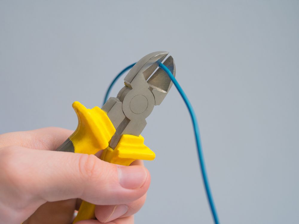 Pessoa utilizando alicate para cortar fio elétrico azul seguindo o Padrão de cores dos fios elétricos ABNT em manutenções elétricas.