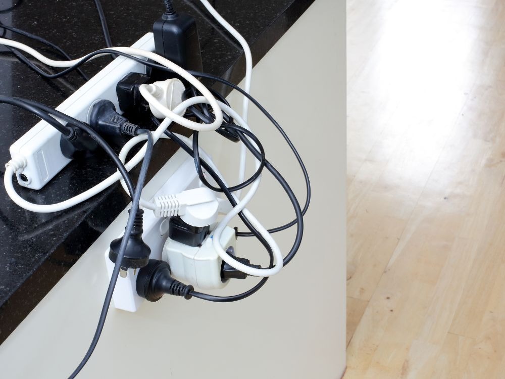 Uma tomada múltipla branca com vários adaptadores e cabos bagunçados conectados, mostrando uma situação de risco de sobrecarga elétrica.