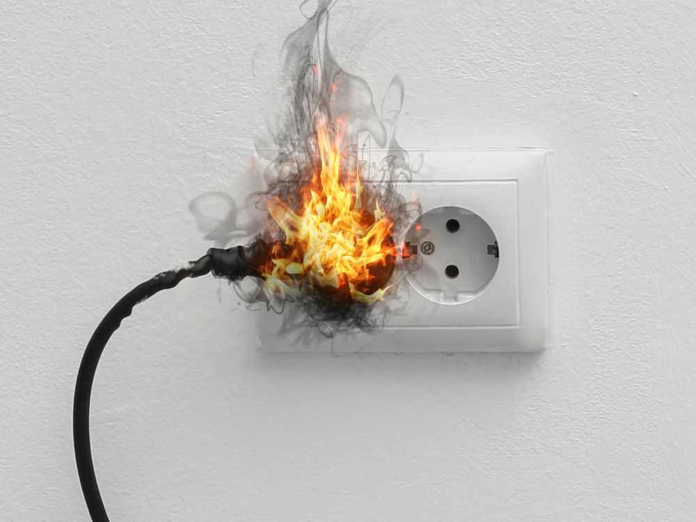 Curto circuito na tomada provocando incêndio no plugue conectado, causado por aquecimento excessivo do fio elétrico.
