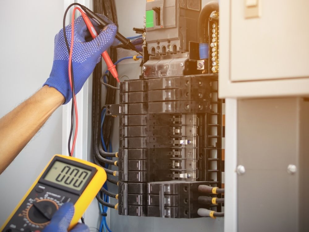 Eletricista utilizando multímetro em painel elétrico, demonstrando Como acontece o curto-circuito durante testes e diagnósticos de falhas elétricas.