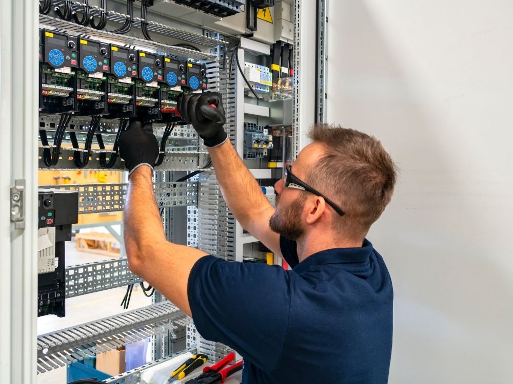 Técnico realizando ajustes em componentes internos, ilustrando o funcionamento e a organização de sistemas industriais ao explicar o que é painel elétrico.