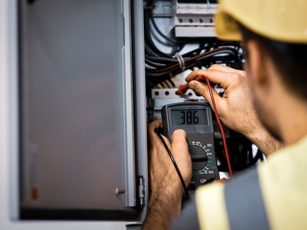 Profissional utilizando multímetro em quadro elétrico, imagem que ajuda a compreender o que é painel elétrico e sua função na distribuição elétrica.