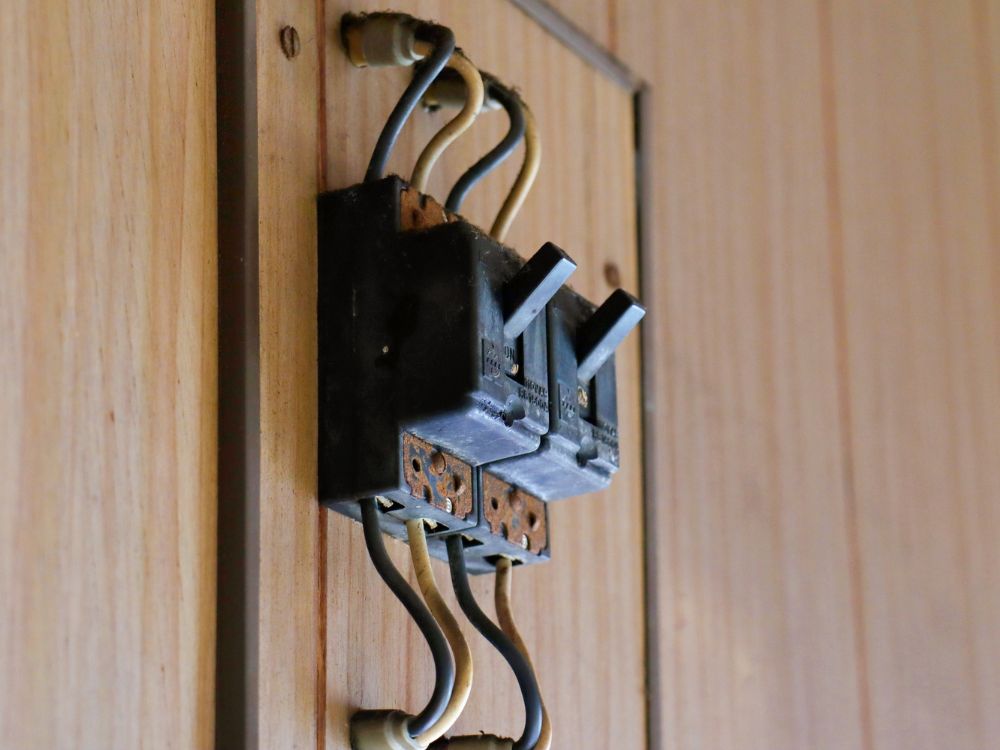 Disjuntores antigos instalados em painel elétrico de madeira, exemplo comum usado para explicar Como saber se o disjuntor queimou em sistemas elétricos antigos.