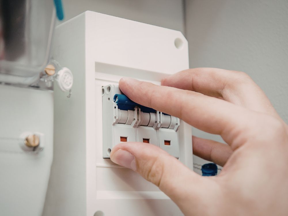 Pessoa acionando disjuntor em quadro de energia, situação comum analisada ao verificar Como saber se o disjuntor queimou em uma instalação elétrica.