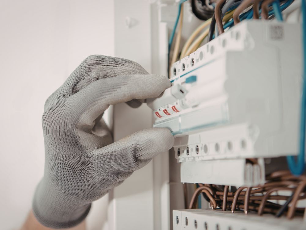 Técnico manipulando disjuntor em quadro de distribuição com luvas de proteção, relacionado a disjuntor desarmando depois de um tempo.
