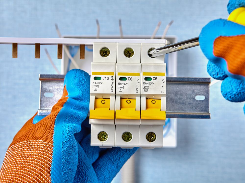 Eletricista ajustando disjuntores em quadro elétrico com ferramentas, ilustrando situações de disjuntor desarmando depois de um tempo.