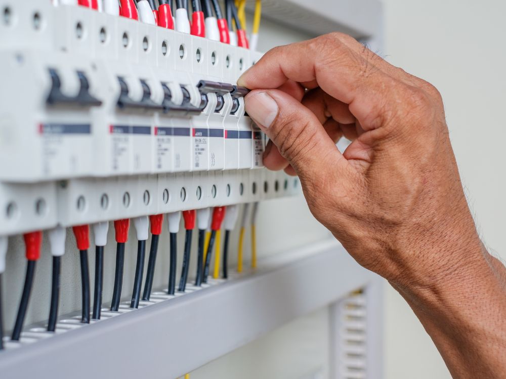 Mão acionando chave de proteção em painel elétrico, imagem que representa a função e a importância do tipo de disjuntor na segurança elétrica.