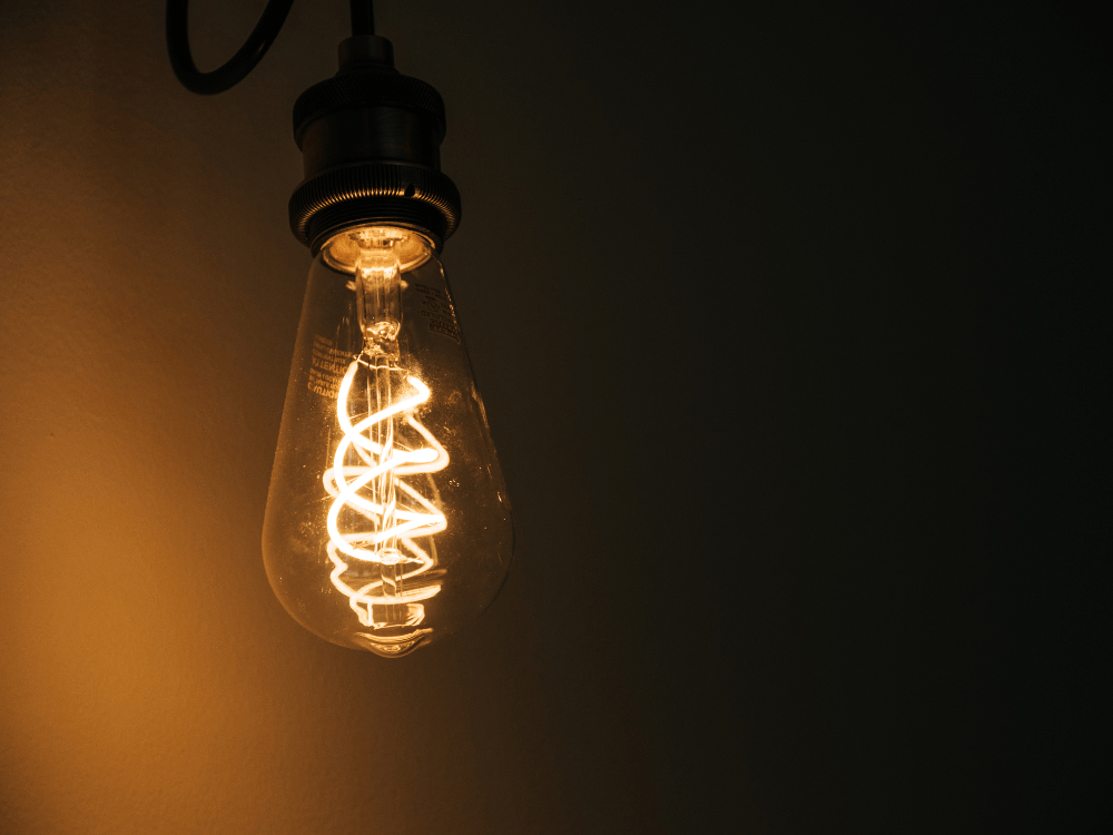 Lâmpada de filamento em estilo retrô acesa exibindo sua espiral interna incandescente com luz alaranjada e fundo escuro.