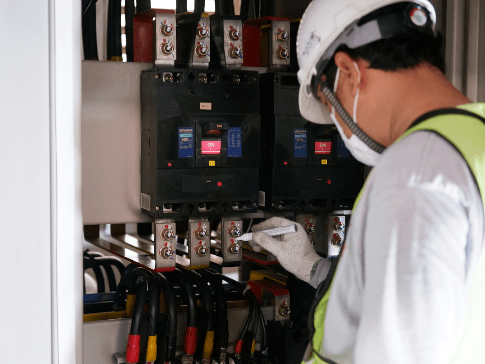 Profissional inspeciona painel elétrico industrial durante manutenção preventiva relacionada ao controle da tensão elétrica.