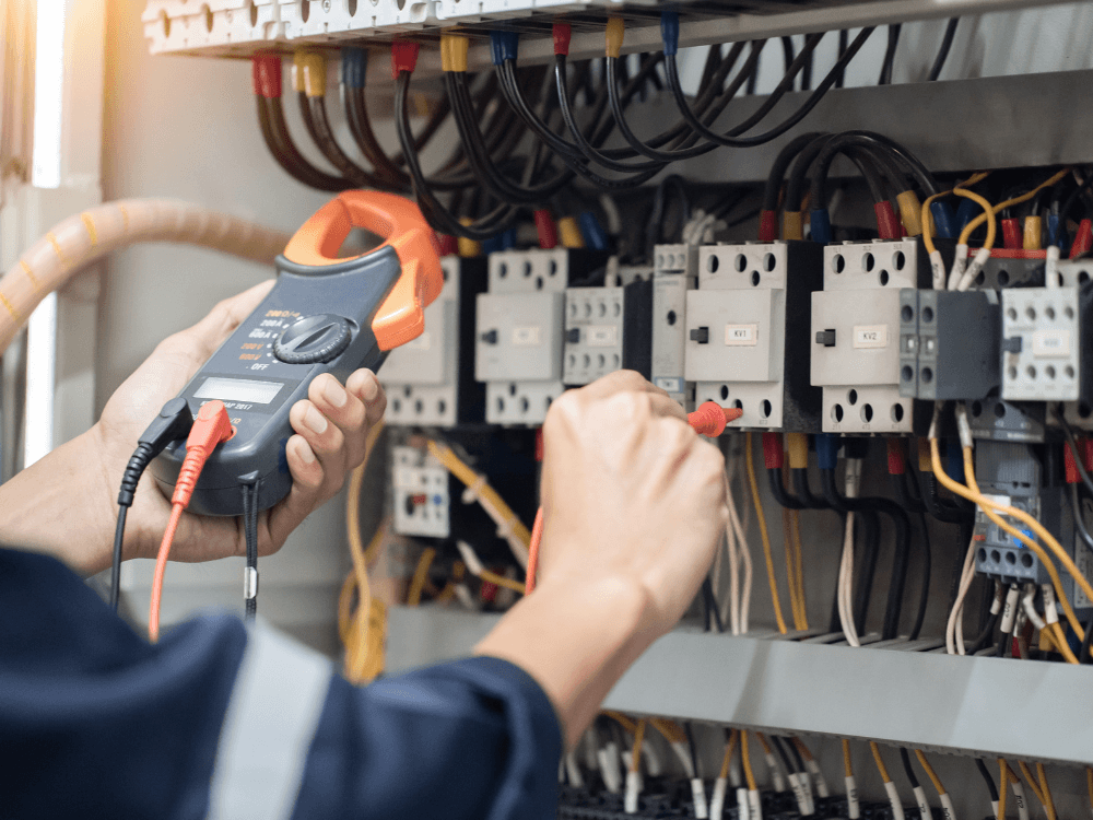 Técnico realiza medição em painel elétrico com alicate amperímetro durante procedimento de verificação da tensão elétrica. Tudo para explicar o que é tensão elétrica.