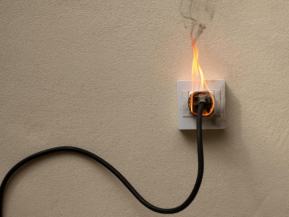 Tomada elétrica com sinais de queima e chamas ao redor do plugue, representando um risco de choque elétrico no imóvel. Tudo para explicar o que é choque elétrico.